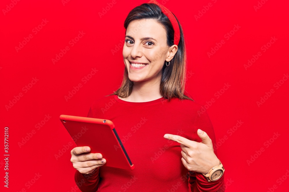 Young beautiful woman holding touchpad smiling happy pointing with hand and finger Young beautiful woman holding touchpad smiling happy pointing with hand and finger