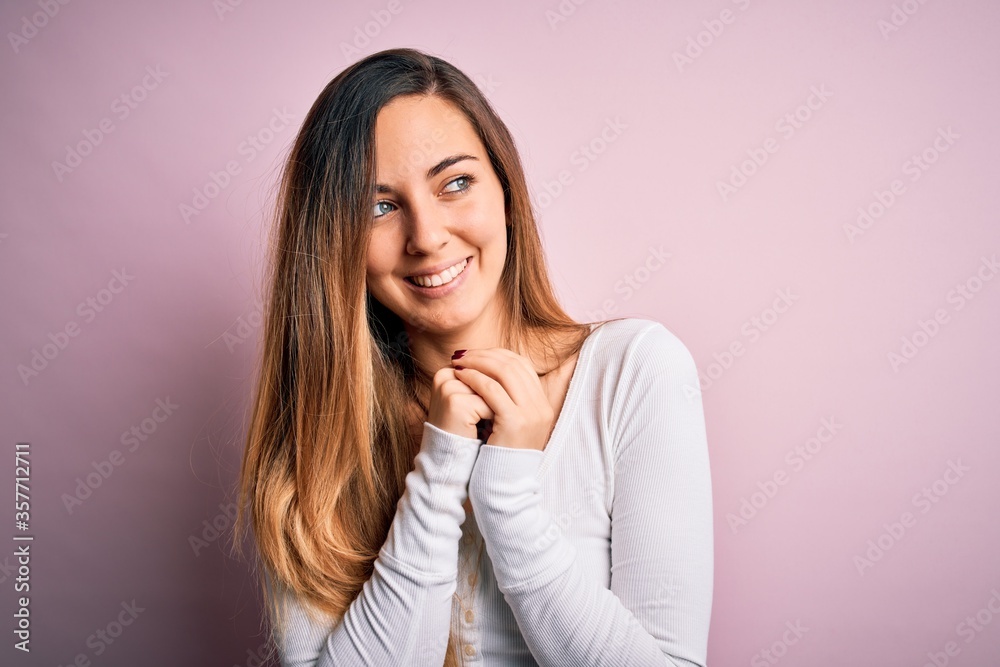 Young beautiful blonde woman with blue eyes wearing white t-shirt over pink background laughing nervous and excited with hands on chin looking to the side Young beautiful blonde woman with blue eyes wearing white t-shirt over pink background laughing nervous and excited with hands on chin looking to the side