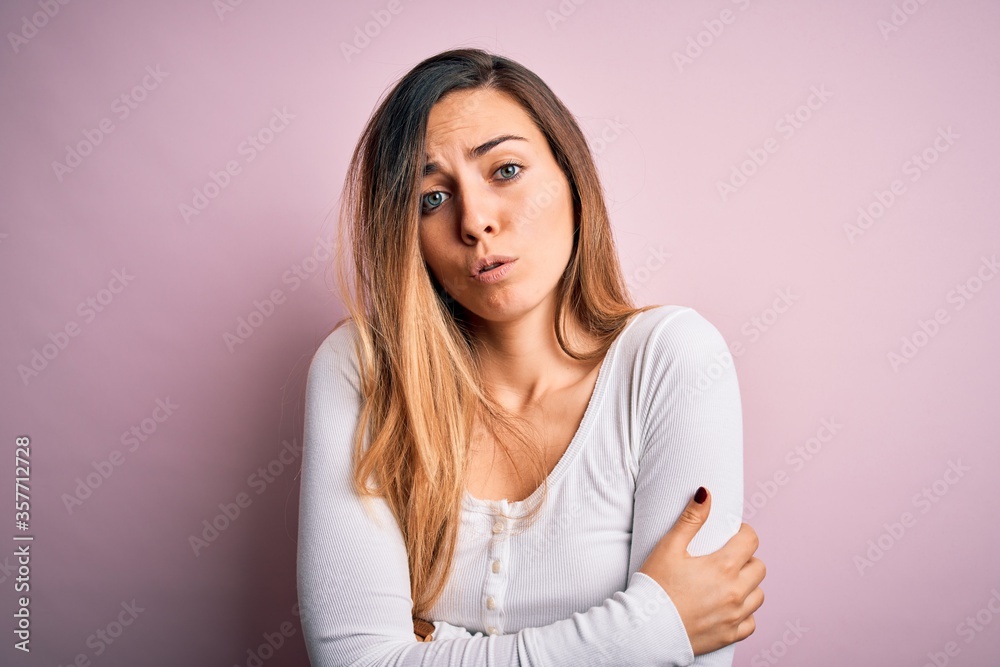 Young beautiful blonde woman with blue eyes wearing white t-shirt over pink background shaking and freezing for winter cold with sad and shock expression on face Young beautiful blonde woman with blue eyes wearing white t-shirt over pink background shaking and freezing for winter cold with sad and shock expression on face