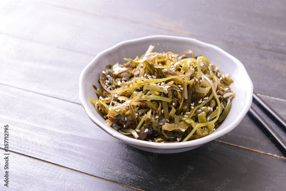 Bowl with tasty seaweed and chopsticks on wooden background