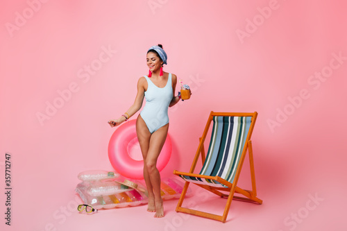 Full length view of tanned lady dancing with cocktail. Stduio shot of graceful young woman in swimsuit. photo
