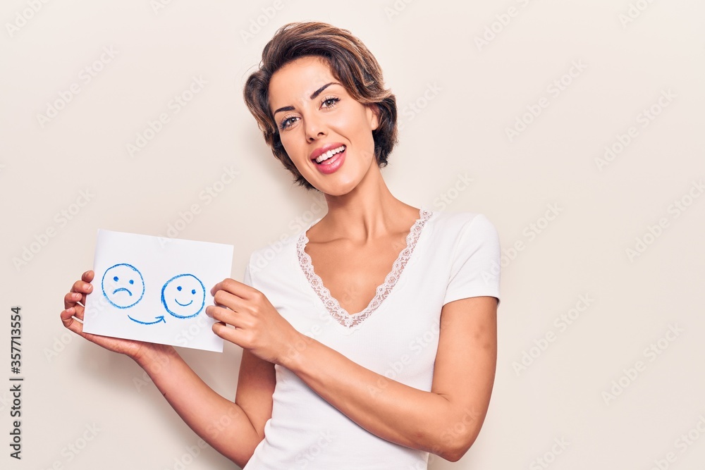 Naklejka premium Young beautiful woman holding sad to happy emotion paper looking positive and happy standing and smiling with a confident smile showing teeth