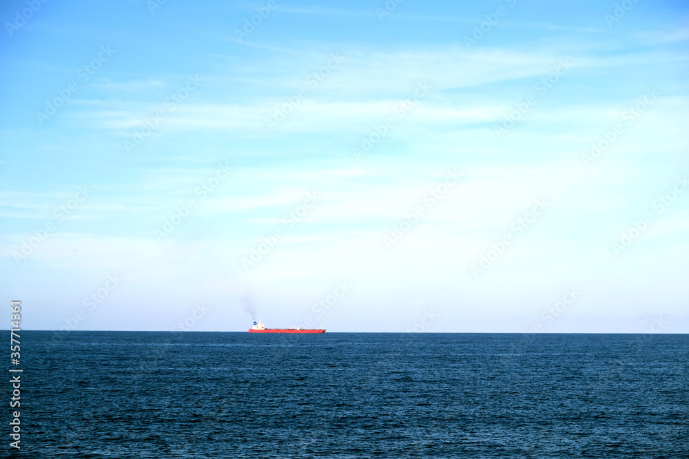 A smoking cargo oil tanker ship on the horizon of blue sea.