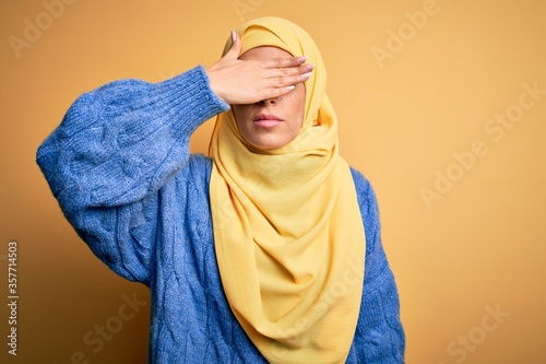 Young beautiful brunette muslim woman wearing arab hijab over isolated yellow background covering eyes with hand, looking serious and sad. Sightless, hiding and rejection concept © Krakenimages.com