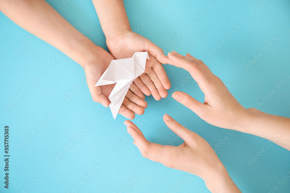 Hands of family with paper dove on color background Hands of family with paper dove on color background
