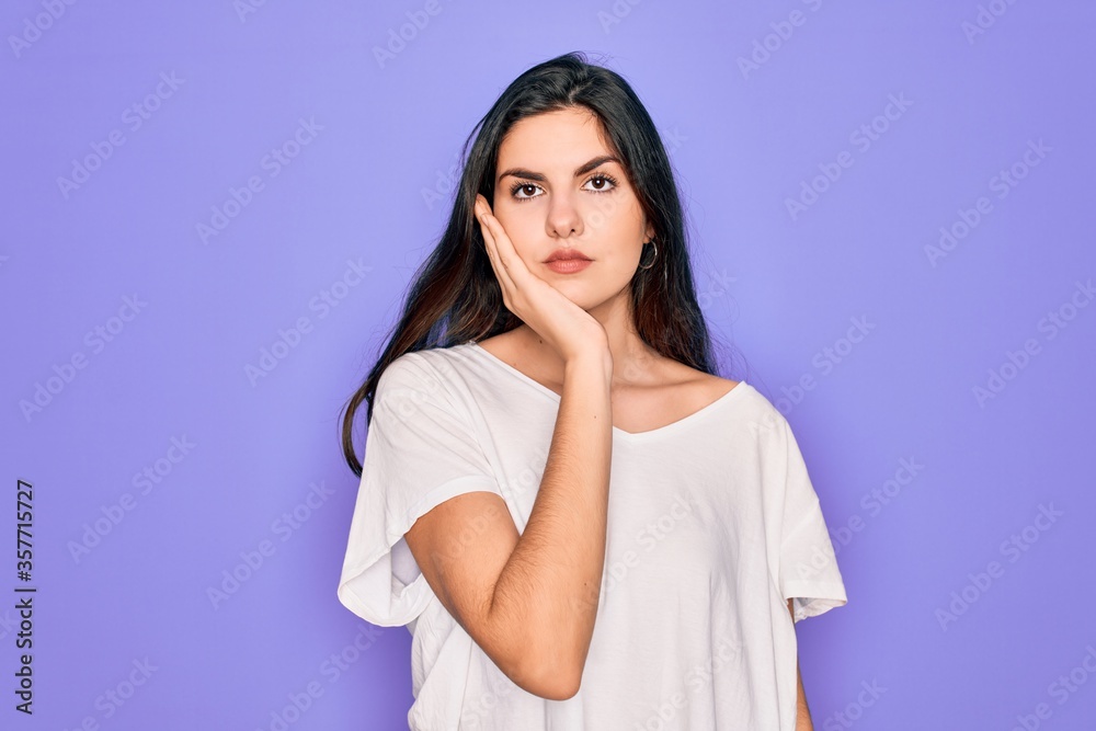 Young beautiful brunette woman wearing casual white t-shirt over purple background thinking looking tired and bored with depression problems with crossed arms. Young beautiful brunette woman wearing casual white t-shirt over purple background thinking looking tired and bored with depression problems with crossed arms.