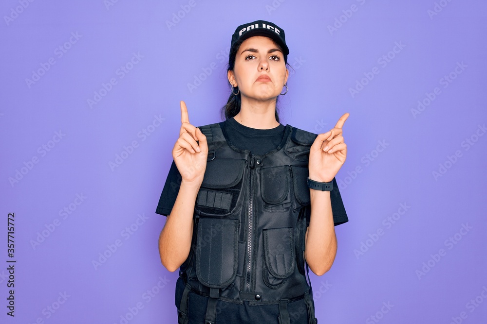 Φωτογραφία Young police woman wearing security bulletproof vest uniform over purple background Pointing up looking sad and upset, indicating direction with fingers, unhappy and depressed