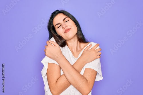 Young beautiful brunette woman wearing casual white t-shirt over purple background Hugging oneself happy and positive, smiling confident. Self love and self care