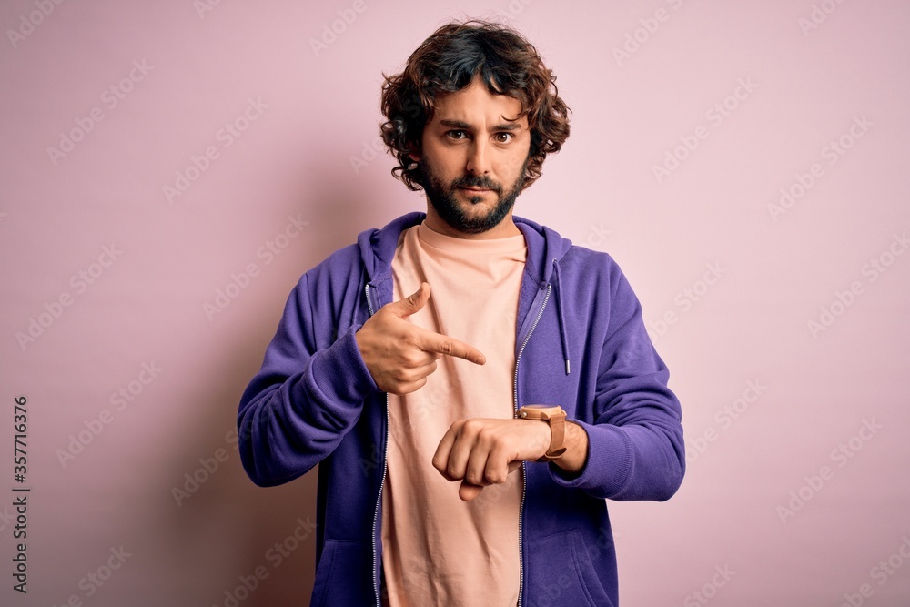 Young handsome sporty man with beard wearing casual sweatshirt over pink background In hurry pointing to watch time, impatience, upset and angry for deadline delay Young handsome sporty man with beard wearing casual sweatshirt over pink background In hurry pointing to watch time, impatience, upset and angry for deadline delay