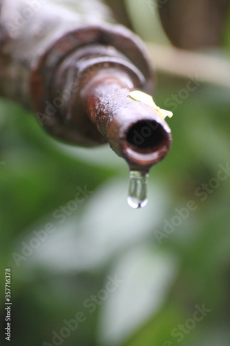 A drop of water dripping from a rusty tap.