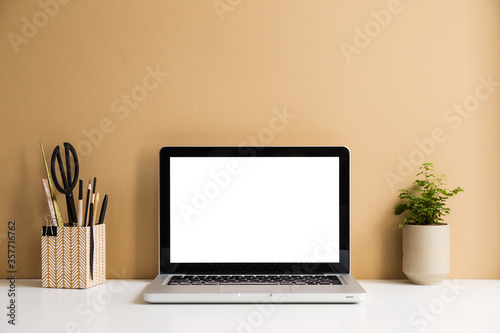 Laptop mockup at stylish workspace with wooden and cork accessories against brght brown wall. photo