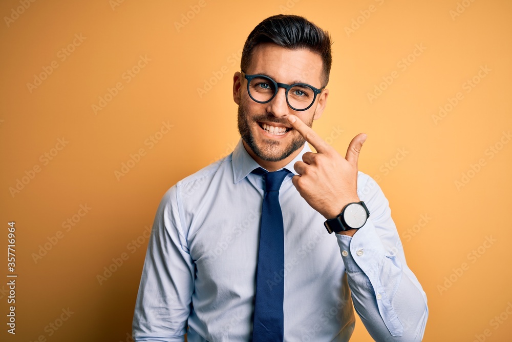 Young handsome businessman wearing tie and glasses standing over yellow background Pointing with hand finger to face and nose, smiling cheerful. Beauty concept Young handsome businessman wearing tie and glasses standing over yellow background Pointing with hand finger to face and nose, smiling cheerful. Beauty concept