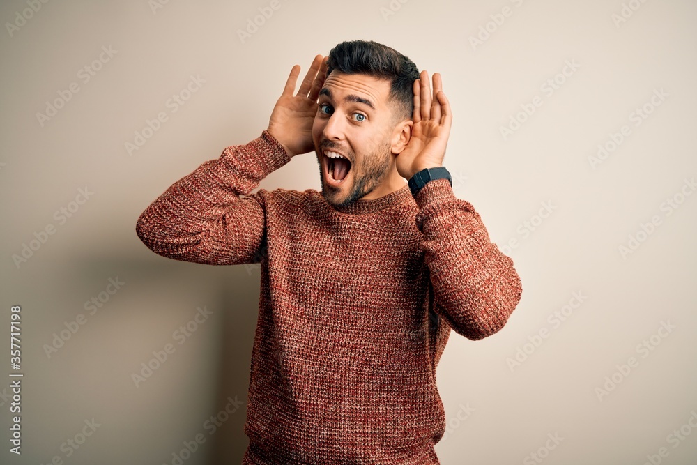 Young handsome man wearing casual sweater standing over isolated white background Smiling cheerful playing peek a boo with hands showing face. Surprised and exited