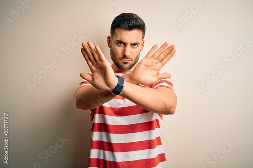 Young handsome man wearing casual striped t-shirt standing over isolated white background Rejection expression crossing arms and palms doing negative sign, angry face