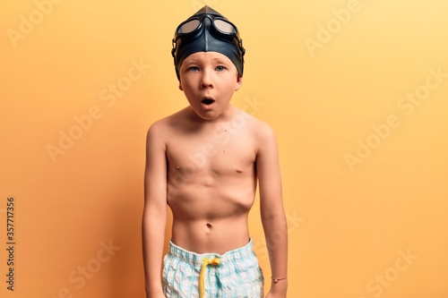 Cute blond kid wearing swimwear and swimmer glasses scared and amazed with open mouth for surprise, disbelief face © Krakenimages.com