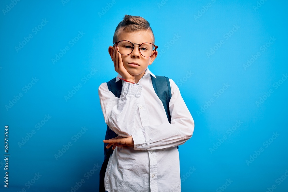 Young little caucasian student kid wearing smart glasses and school bag over blue background thinking looking tired and bored with depression problems with crossed arms. Young little caucasian student kid wearing smart glasses and school bag over blue background thinking looking tired and bored with depression problems with crossed arms.