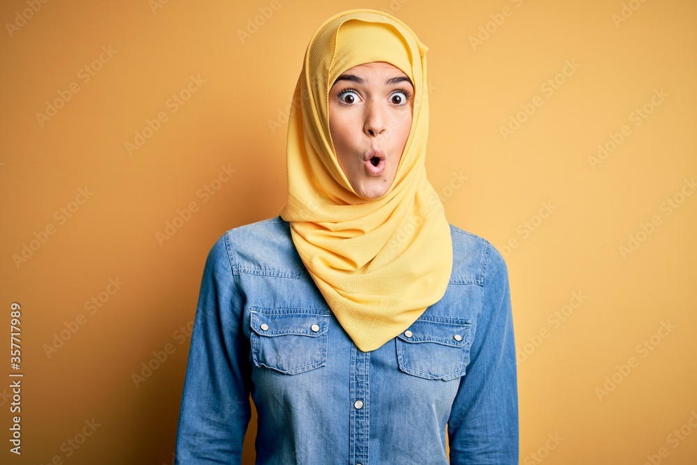 Young beautiful girl wearing muslim hijab standing over isolated yellow background afraid and shocked with surprise expression, fear and excited face. Young beautiful girl wearing muslim hijab standing over isolated yellow background afraid and shocked with surprise expression, fear and excited face.