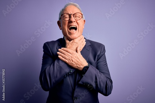 Grey haired senior business man wearing glasses and elegant suit and tie over purple background shouting suffocate because painful strangle. Health problem. Asphyxiate and suicide concept.
