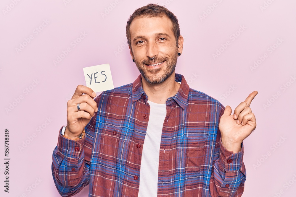 Fototapeta premium Young handsome man holding yes reminder smiling happy pointing with hand and finger to the side
