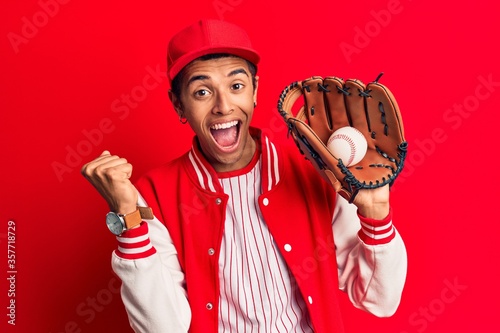 Young african amercian man wearing baseball uniform holding golve and ball screaming proud, celebrating victory and success very excited with raised arms photo