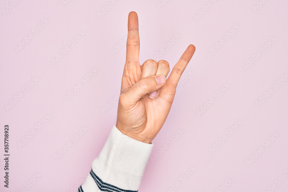 Hand of caucasian young man showing fingers over isolated pink background gesturing rock and roll symbol, showing obscene horns gesture