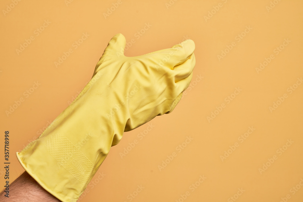 Hand of caucasian young man with cleaning glove over isolated yellow background holding invisible object, empty hand doing clipping and grabbing gesture Hand of caucasian young man with cleaning glove over isolated yellow background holding invisible object, empty hand doing clipping and grabbing gesture