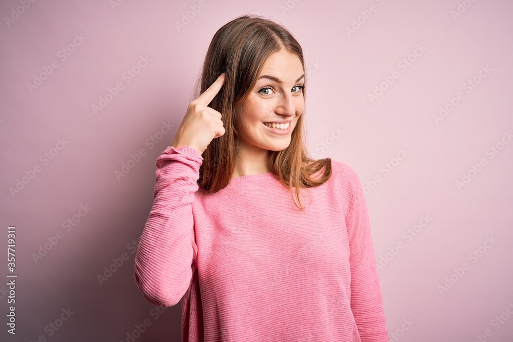 Young beautiful redhead woman wearing casual sweater over isolated pink background Smiling pointing to head with one finger, great idea or thought, good memory Young beautiful redhead woman wearing casual sweater over isolated pink background Smiling pointing to head with one finger, great idea or thought, good memory