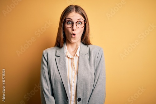 Fotografía Young beautiful redhead woman wearing jacket and glasses over isolated yellow background afraid and shocked with surprise expression, fear and excited face