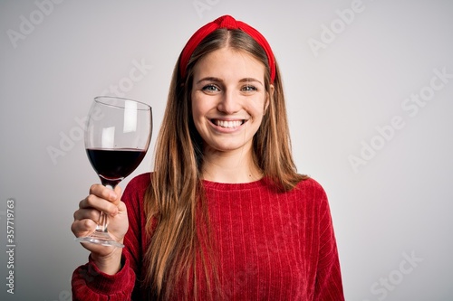Fotografia Young beautiful redhead woman drinking glass of red wine over isolated white bac
