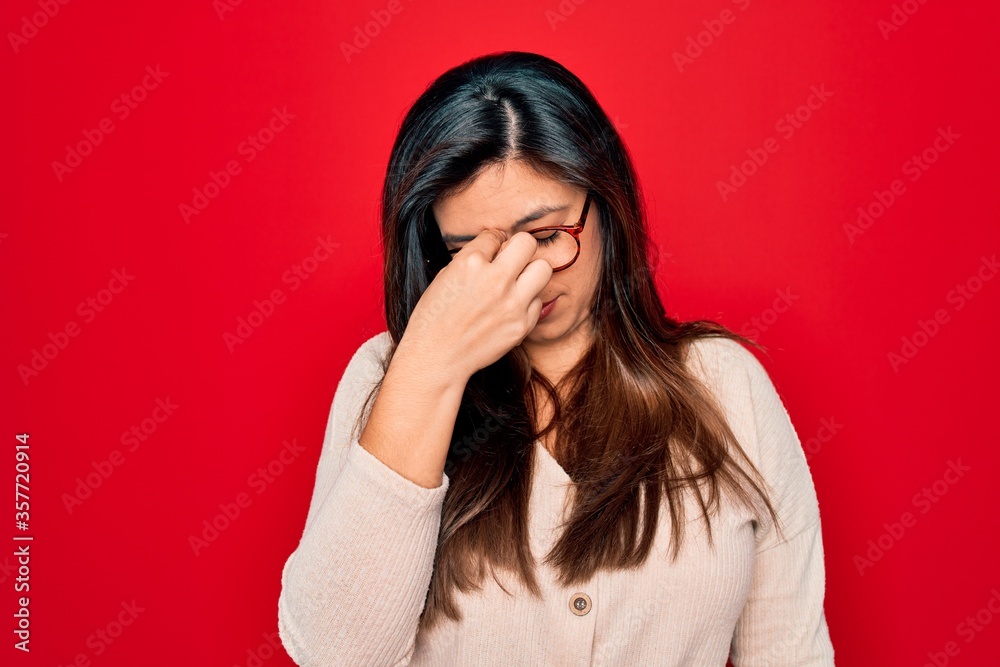 Young hispanic smart woman wearing glasses standing over red isolated background tired rubbing nose and eyes feeling fatigue and headache. Stress and frustration concept. Young hispanic smart woman wearing glasses standing over red isolated background tired rubbing nose and eyes feeling fatigue and headache. Stress and frustration concept.