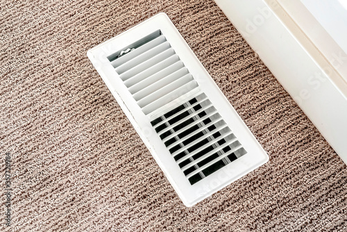 фотографія White air conditioner duct grille cover against floor with brown carpet