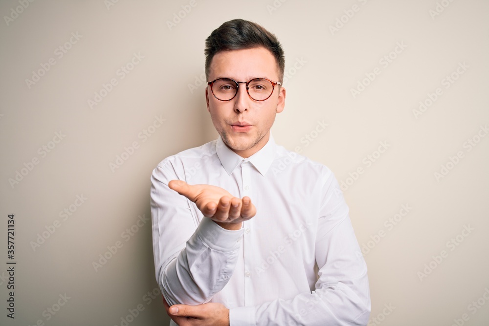 Young handsome business mas wearing glasses and elegant shirt over isolated background looking at the camera blowing a kiss with hand on air being lovely and sexy. Love expression. Young handsome business mas wearing glasses and elegant shirt over isolated background looking at the camera blowing a kiss with hand on air being lovely and sexy. Love expression.