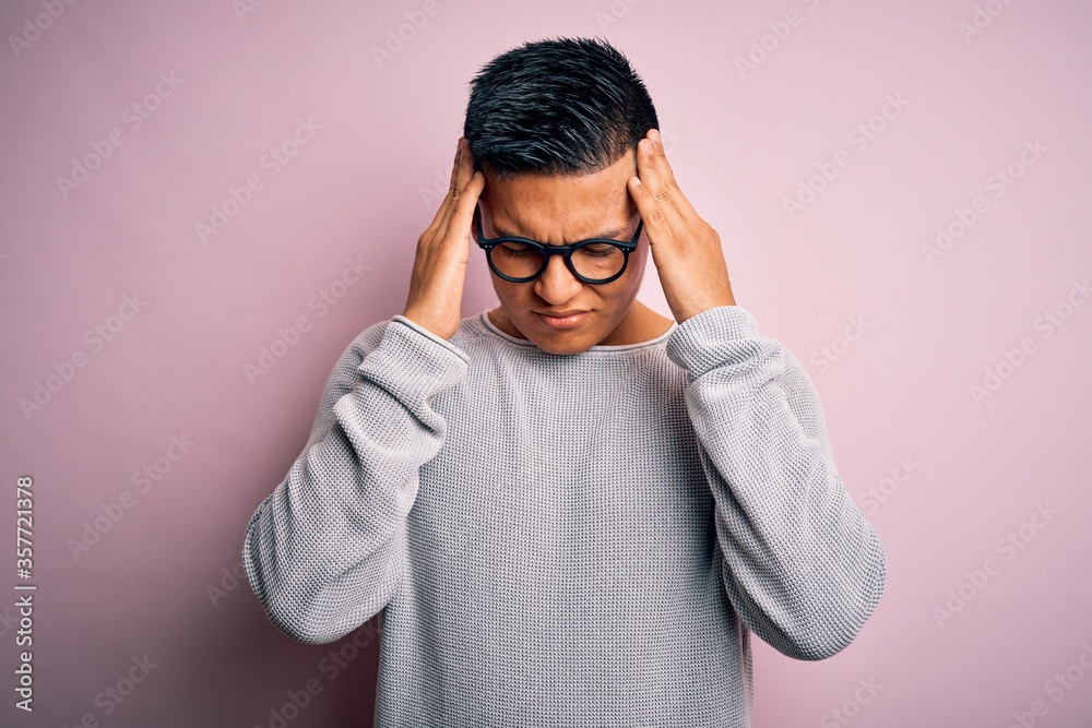 Young handsome latin man wearing casual sweater and glasses over pink background suffering from headache desperate and stressed because pain and migraine. Hands on head. Young handsome latin man wearing casual sweater and glasses over pink background suffering from headache desperate and stressed because pain and migraine. Hands on head.