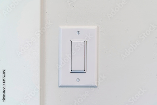 Electrical rocker light switch with flat broad lever on white interior wall