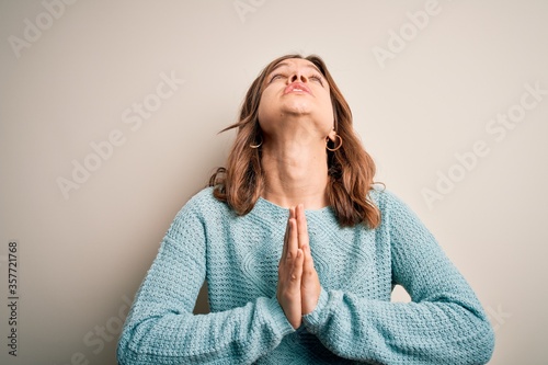 Young blonde girl wearing casual blue winter sweater over isolated background begging and praying with hands together with hope expression on face very emotional and worried. Begging.