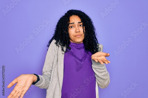 Young african american sporty woman wearing casual sweatshirt over purple background clueless and confused expression with arms and hands raised. Doubt concept. © Krakenimages.com