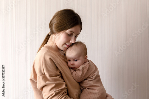 Cheerful beautiful young woman holding baby girl in her hands and looking at her with love at home