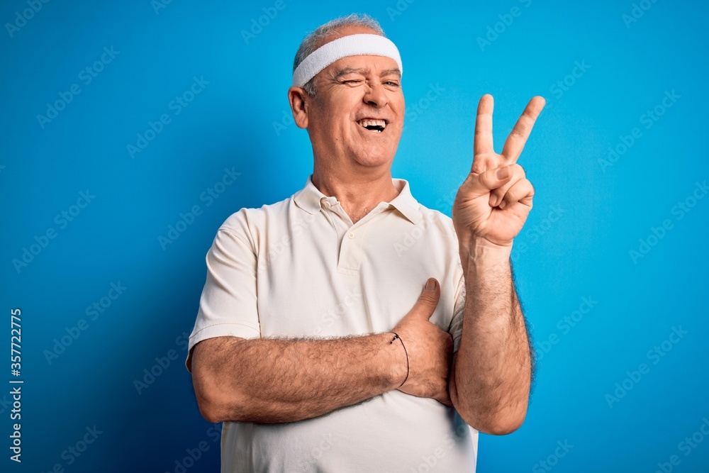 Middle age hoary sportsman doing sport wearing sportswear over isolated blue background smiling with happy face winking at the camera doing victory sign. Number two. Middle age hoary sportsman doing sport wearing sportswear over isolated blue background smiling with happy face winking at the camera doing victory sign. Number two.