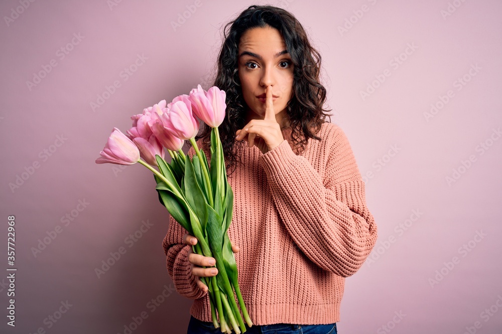 Young beautiful romantic woman with curly hair holding bouquet of pink tulips asking to be quiet with finger on lips. Silence and secret concept. Young beautiful romantic woman with curly hair holding bouquet of pink tulips asking to be quiet with finger on lips. Silence and secret concept.
