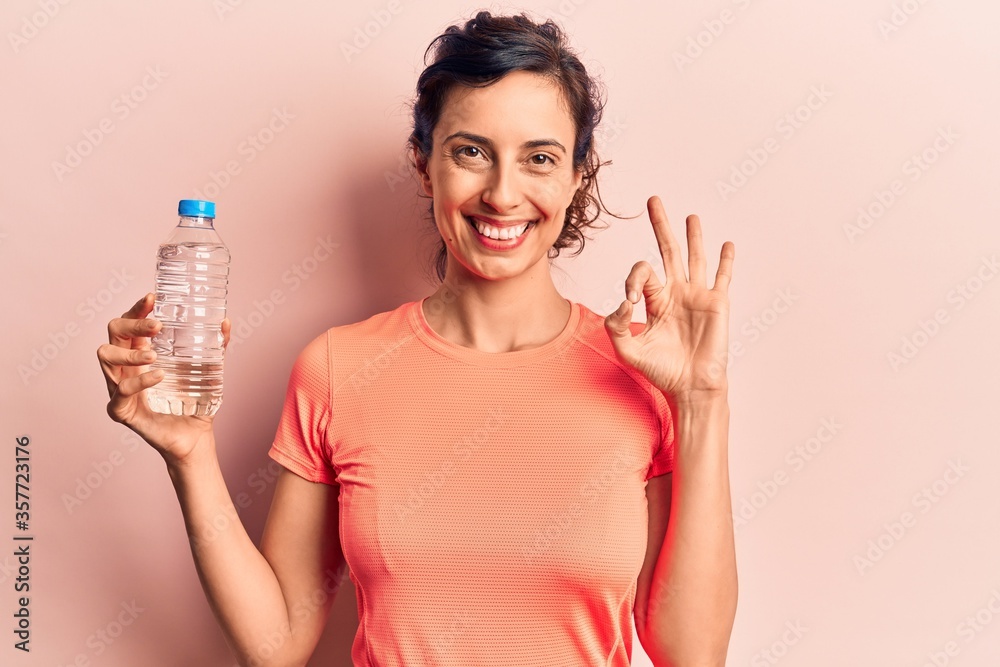 Young beautiful hispanic woman drinking bottle of water doing ok sign with fingers, smiling friendly gesturing excellent symbol Young beautiful hispanic woman drinking bottle of water doing ok sign with fingers, smiling friendly gesturing excellent symbol