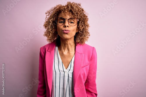 Young african american businesswoman wearing glasses standing over pink background looking at the camera blowing a kiss on air being lovely and sexy. Love expression.