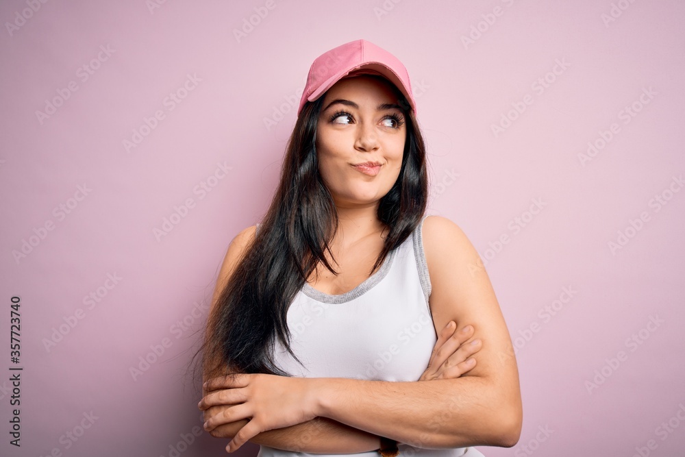 Young brunette woman wearing casual sport cap over pink background smiling looking to the side and staring away thinking.