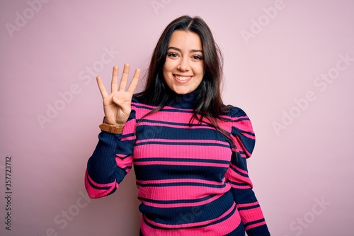 Young brunette elegant woman wearing striped shirt over pink isolated background showing and pointing up with fingers number four while smiling confident and happy. © Krakenimages.com