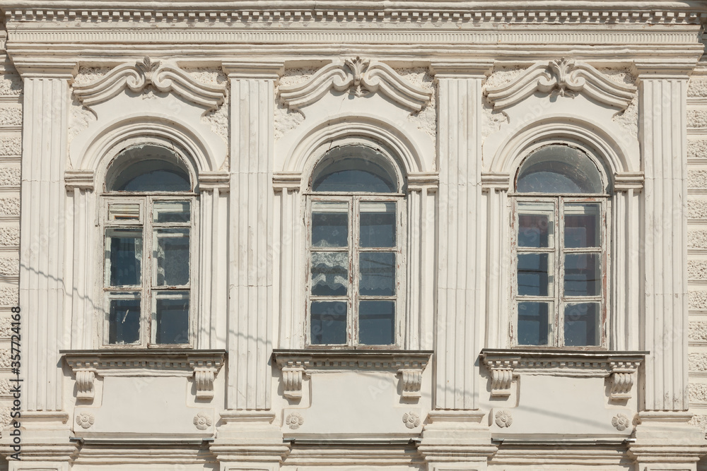 Fragment of the front of an old house with three windows framed by a stucco pattern