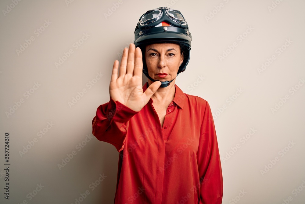 Middle age motorcyclist woman wearing motorcycle helmet over isolated white background doing stop sing with palm of the hand. Warning expression with negative and serious gesture on the face. Middle age motorcyclist woman wearing motorcycle helmet over isolated white background doing stop sing with palm of the hand. Warning expression with negative and serious gesture on the face.