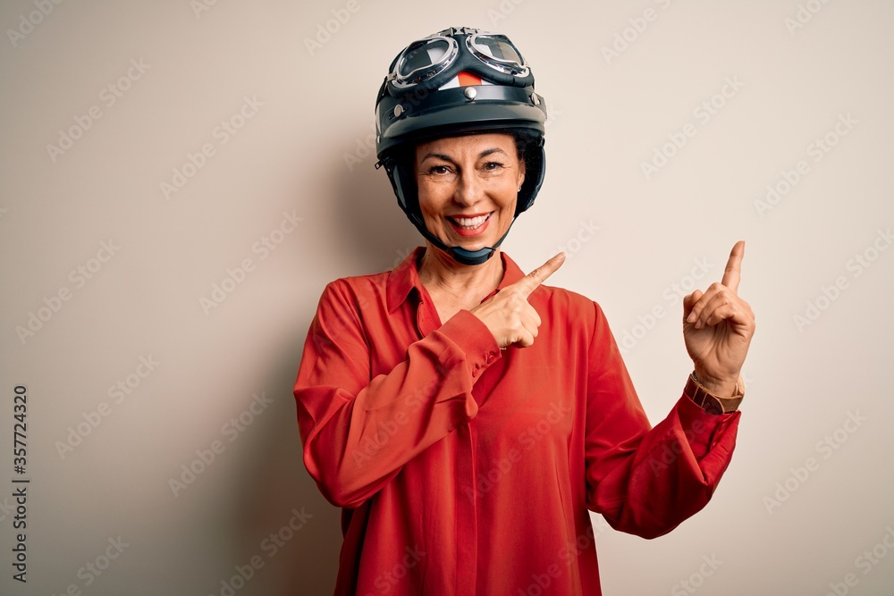 Middle age motorcyclist woman wearing motorcycle helmet over isolated white background smiling and looking at the camera pointing with two hands and fingers to the side. Middle age motorcyclist woman wearing motorcycle helmet over isolated white background smiling and looking at the camera pointing with two hands and fingers to the side.