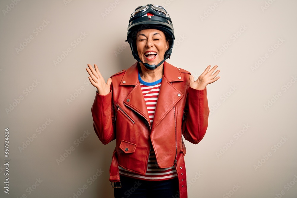 Middle age motorcyclist woman wearing motorcycle helmet and jacket over white background celebrating mad and crazy for success with arms raised and closed eyes screaming excited. Winner concept Middle age motorcyclist woman wearing motorcycle helmet and jacket over white background celebrating mad and crazy for success with arms raised and closed eyes screaming excited. Winner concept