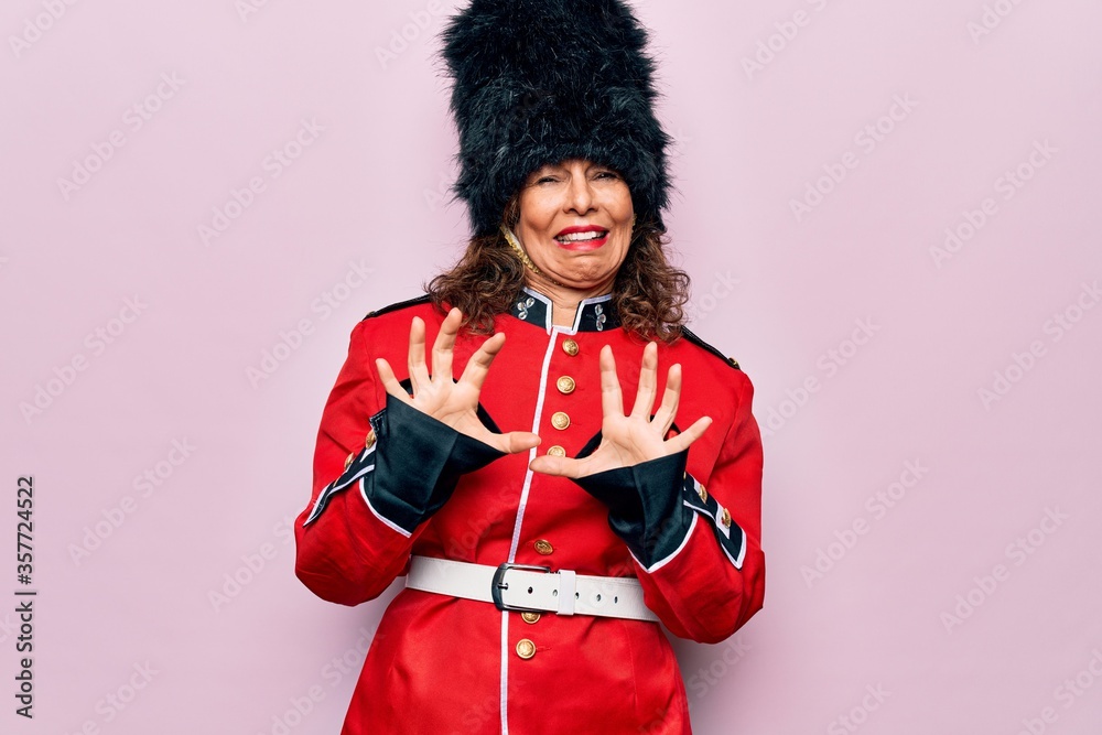 Middle age beautiful wales guard woman wearing traditional uniform over pink background disgusted expression, displeased and fearful doing disgust face because aversion reaction. With hands raised