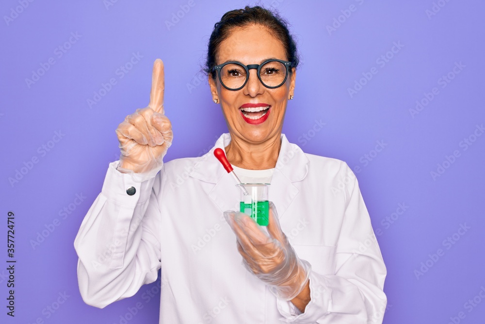 Middle age senior scientist woman wearing laboratory coat holding research test tube surprised with an idea or question pointing finger with happy face, number one