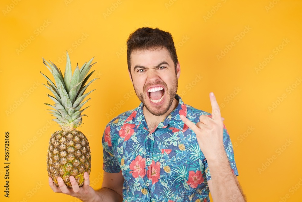 Obraz premium Born to rock this world. Joyful man in fashionable clothes screaming out loud and showing with raised arms horns or rock gesture, expressing excitement of being on concert of band.